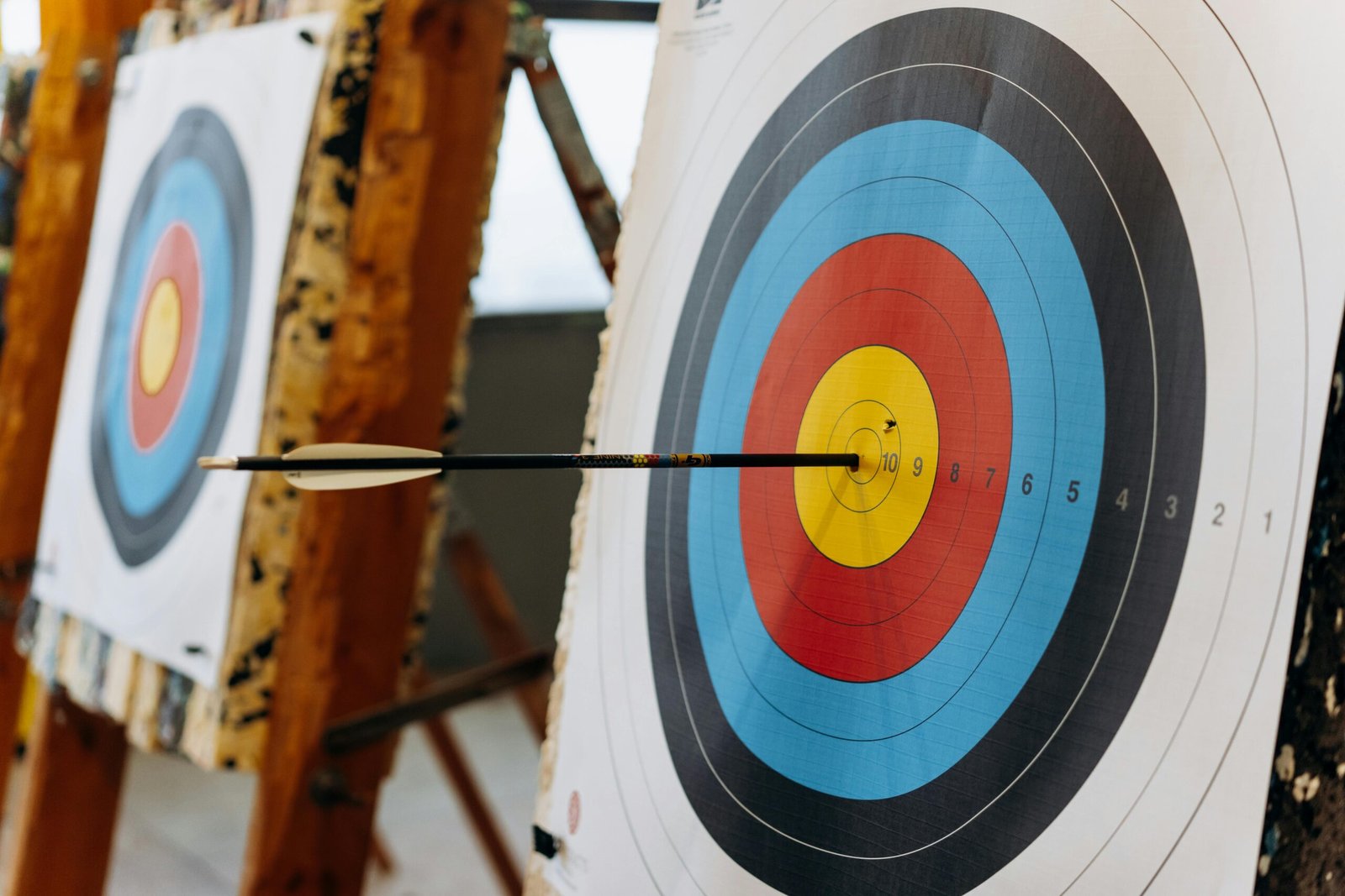 An arrow hits the bullseye on a colorful target in an indoor archery range.